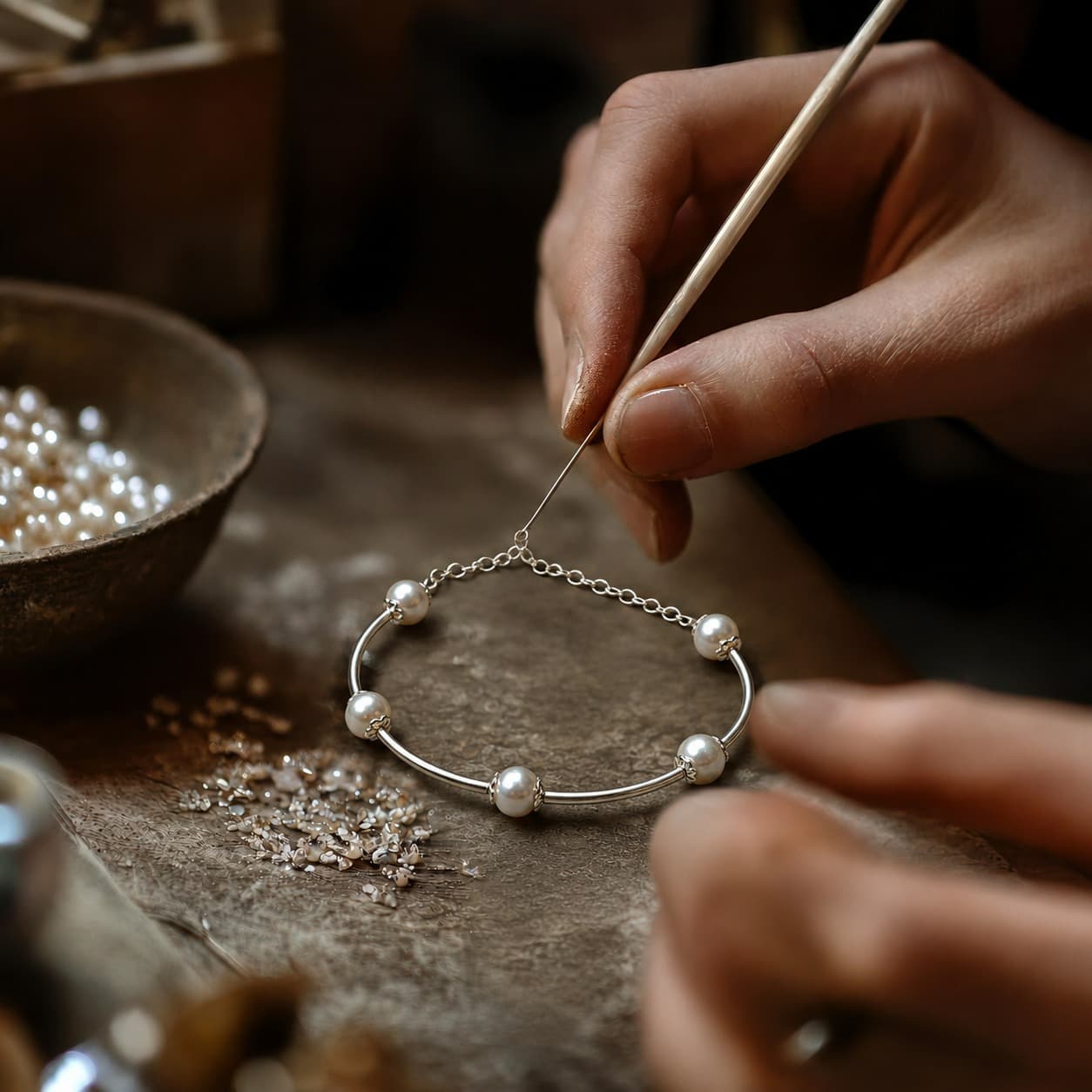A karigar's hands crafting a pearl bracelet