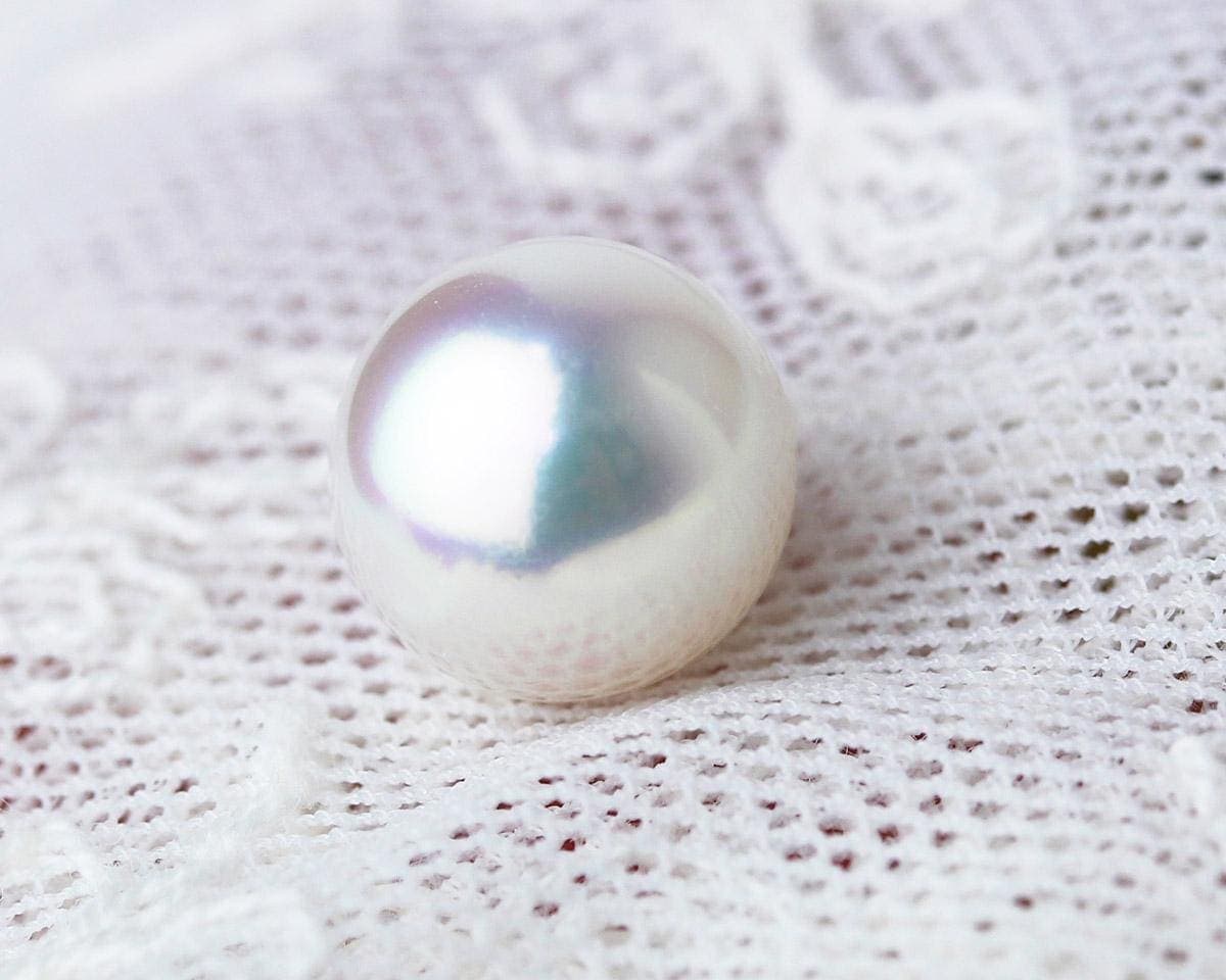 A single luminous Akoya pearl on lace